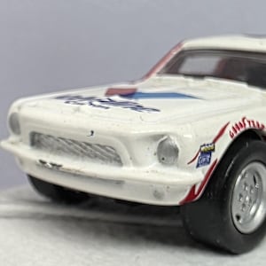 May include: A vintage toy race car in white, red, and blue. The car features the number 6 on the side and various sponsor decals. The tires are black, and the wheels are silver.