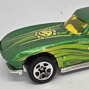 Op de afbeelding: Groene speelgoedauto met een hardtop en geel getinte ramen. De auto heeft zwarte wielen en een zilveren uitlaatpijp. De auto heeft de tekst "Funky Vibes" en een smiley-logo.