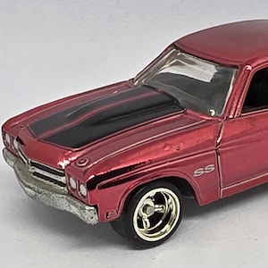 May include: A red die-cast model car with a black stripe on the hood. The car has gold-colored rims and the letters "SS" on the side. The car is a classic muscle car.
