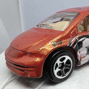 May include: A red toy minivan with black wheels and a soccer-themed graphic on the side. The van has a sunroof and the word "GOAALLL" is visible on the side. The toy is a Dodge model.