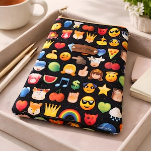 May include: Black zippered pouch with a gold zip, covered in emoji and cartoon graphics. The pouch has a small leather tag that reads "CUNTY!!!". The design includes hearts, crowns, and smiling faces, with a rainbow.