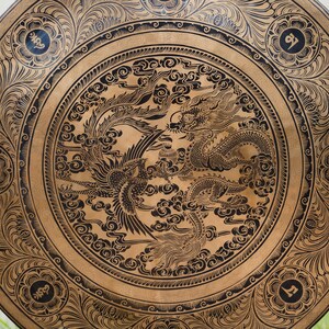 Peut inclure: Objet d&eacute;coratif rond en bois avec un motif d&eacute;taill&eacute; de dragon et de ph&eacute;nix noirs. L'&oelig;uvre d'art est pos&eacute;e sur un fond brun clair, avec des accents floraux et calligraphiques sur les bords. Le diam&egrave;tre est d'environ 61 cm.