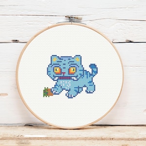 Könnte beinhalten: Kreuzstich-Stickerei in einem Holzreifen. Das Design zeigt eine hellblaue Cartoon-Katze mit orangefarbenen Augen und einem kleinen grünen und braunen Objekt. Der Hintergrund ist weiß.