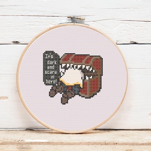 Puede incluir: Bordado de punto de cruz en un aro de madera. El diseño presenta un cofre del tesoro con la boca muy abierta y el texto "It's dark and scary in here!" en un bocadillo. El cofre es marrón y rojo.