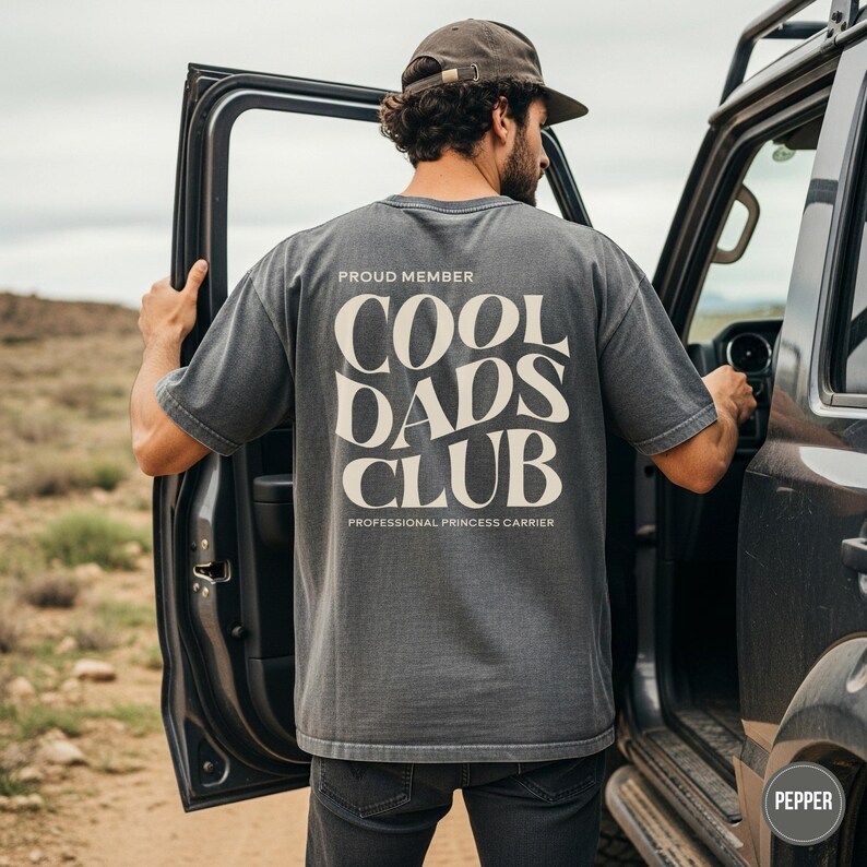 Back view of an pepper Comfort Colors shirt featuring a large cream Cool Dads Club graphic and Professional Princess Carrier wording.