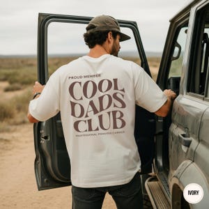 Back view of an ivory Comfort Colors shirt featuring a large taupe Cool Dads Club graphic and Professional Princess Carrier wording.