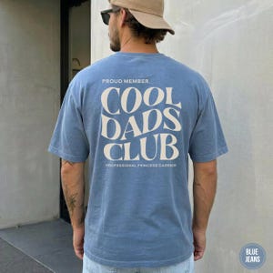 Back view of a Blue Jean Comfort Colors t-shirt with a large cream Cool Dads Club graphic printed on the back.