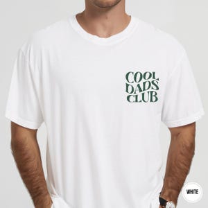 Front view of a white Comfort Colors t-shirt featuring a small green Cool Dads Club graphic on the left chest.