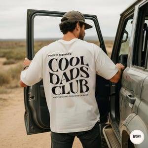 Back view of an ivory t-shirt displaying a large black Cool Dads Club design with Professional Princess Carrier text underneath.