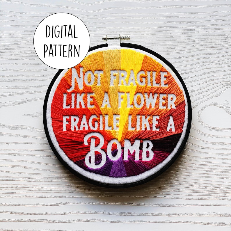 May include: A colourful embroidery hoop with the text "Not Fragile Like A Flower Fragile Like A Bomb". The embroidery is done in a rainbow colour scheme with yellow, orange, red, purple, and white thread.
