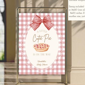 Könnte beinhalten: Ein Schild mit rosa Vichy-Hintergrund und einer dekorativen Schleife oben. Auf dem Schild steht "A Little Cutie Pie Is On The Way" mit einer Tortengrafik. Das Schild ist für eine Babyparty und ist eine editierbare Vorlage.