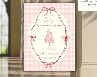 May include: A pink and white gingham baby shower sign with the text "Baby it's cold outside" and "Welcome to Annabelle's Baby Shower!" The sign is framed with a red oval and bows. The sign is displayed on a gold metal stand.