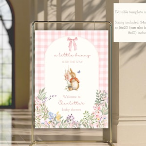 May include: A pink and white gingham baby shower sign with the text "a little bunny is on the way." The sign features a watercolor illustration of a bunny, flowers, and the text "Welcome to Charlotte's baby shower."