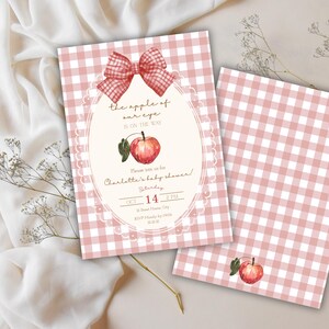 May include: Baby shower invitation with a pink gingham pattern. The invitation features a watercolor apple illustration, a red bow, and the text "the apple of our eye is on the way." The date and time of the shower are also included.