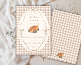 May include: A set of two birthday invitations with a tan and white gingham pattern. The front invitation features an oval frame with the text "a little turkey is turning one!" and a watercolor illustration of a roasted turkey. The back invitation has the same gingham pattern.