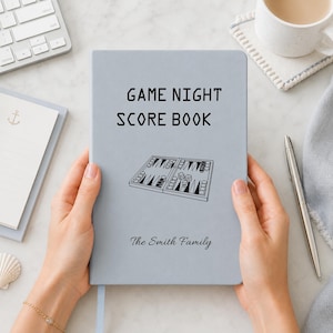May include: A light blue rectangular score book with the text GAME NIGHT SCORE BOOK printed in black, featuring a line art illustration of an open backgammon board with dice and checkers, and the custom text The Smith Family at the bottom.