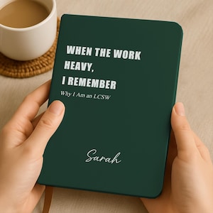 Könnte beinhalten: Ein dunkelgrünes Notizbuch mit dem Text "WHEN THE WORK HEAVY, I REMEMBER Why I Am an LCSW" in Weiß. Der Name "Sarah" ist unten in Kursivschrift geschrieben. Eine Tasse Kaffee befindet sich im Hintergrund.