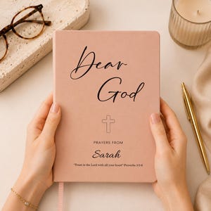 Peut inclure: Un journal de prière couleur rose poudré avec un texte noir indiquant Dear God, suivi d'une icône de croix, les mots PRAYERS FROM, le prénom Sarah, et le verset Trust in the Lord with all your heart Proverbs 3:5-6 sur la couverture.