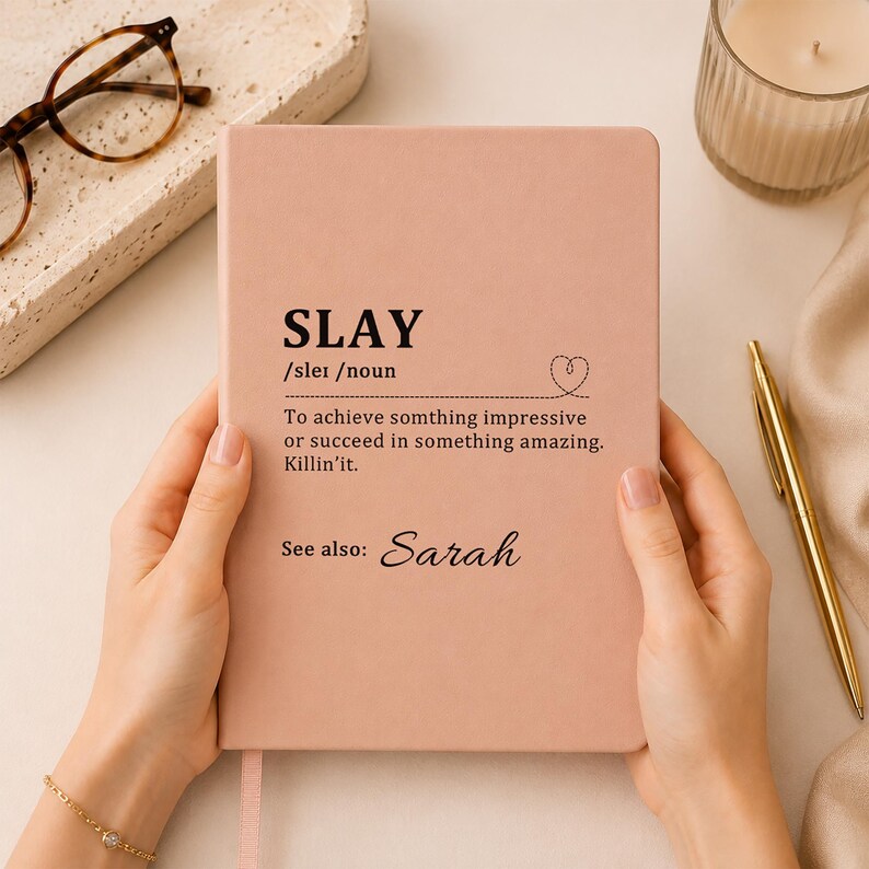 May include: A dusty rose notebook featuring the black printed definition of the word SLAY, which reads: To achieve somthing impressive or succeed in something amazing. Killin'it. Below the definition, the text reads: See also: Sarah.