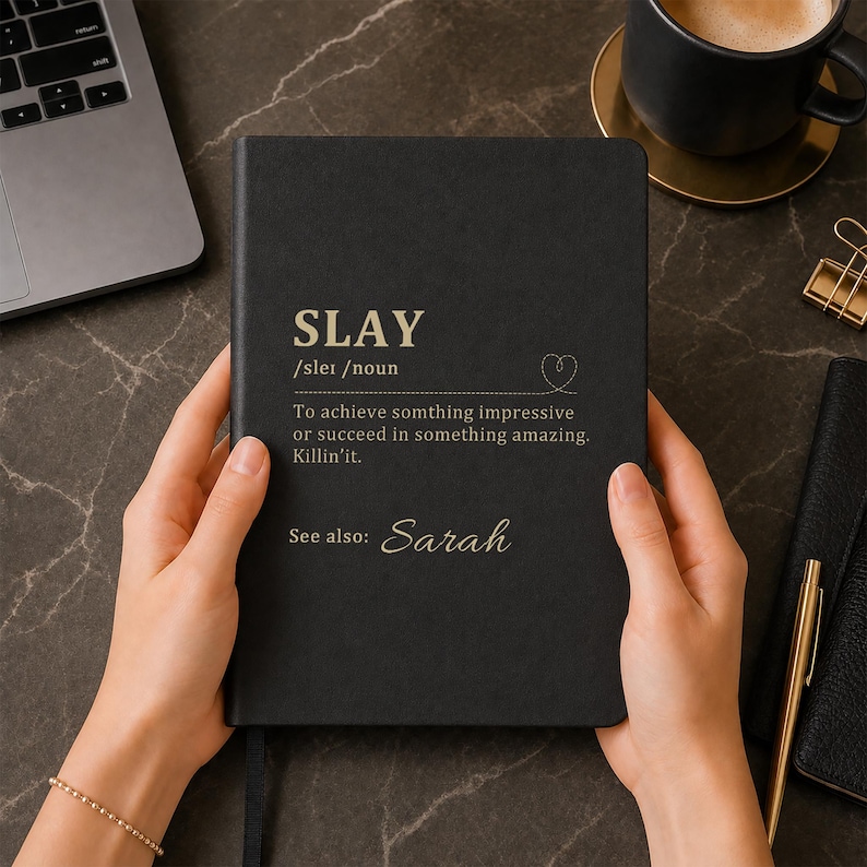May include: A black hardcover notebook featuring gold-colored text that defines the word SLAY as achieving something impressive or succeeding in something amazing, with the name Sarah printed below as a reference, all in a clean, professional layout.