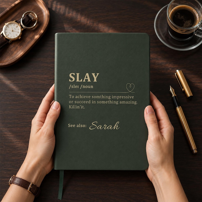 May include: A dark green hardcover notebook with gold text that reads SLAY /sleɪ /noun To achieve somthing impressive or succeed in something amazing. Killin'it. See also: Sarah. The notebook features a small heart icon and a green ribbon bookmark.