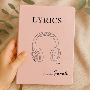 Könnte beinhalten: Ein rosa Notizbuch mit dem Wort „LYRICS“ in schwarzen Großbuchstaben oben. Darunter befindet sich eine schwarze Strichzeichnung eines Kopfhörers. Die Worte „Written by: Sarah“ stehen unten auf dem Notizbuch.