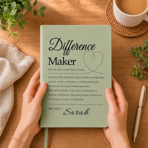 May include: A sage green notebook featuring the text "Difference Maker" with a phonetic pronunciation, a definition of the term, a dashed heart outline, and the name "Sarah" printed at the bottom in a black serif and script font.