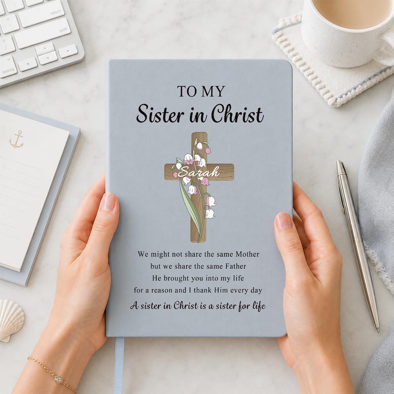 May include: A light blue notebook featuring the text TO MY SISTER IN CHRIST, a wooden cross illustration with lily of the valley flowers, the name Sarah, and a poem that reads: We might not share the same Mother but we share the same Father.