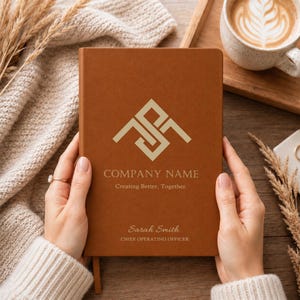 May include: A brown leather-bound notebook featuring a gold geometric logo at the top, the text COMPANY NAME, the slogan Creating Better, Together., and the name Sarah Smith with the title CHIEF OPERATING OFFICER printed in gold lettering.