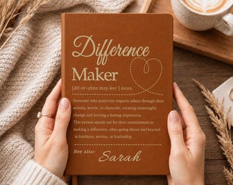 Può includere: Un taccuino marrone con il testo Difference Maker, una definizione del termine, un contorno di cuore tratteggiato e il nome Sarah stampati in un colore chiaro sulla copertina. Il taccuino è tenuto da due mani su uno sfondo neutro.