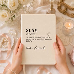 May include: A cream-colored notebook featuring the black printed text SLAY, the phonetic spelling, and the definition: To achieve somthing impressive or succeed in something amazing. Killin'it. Below the definition, the text reads: See also: Sarah.