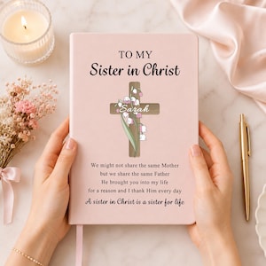 May include: A light pink journal featuring the text TO MY Sister in Christ, a wooden cross graphic with lily of the valley flowers, the name Sarah, and a poem that reads We might not share the same Mother but we share the same Father.