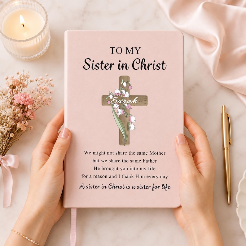 May include: A light pink journal featuring the text TO MY Sister in Christ, a wooden cross graphic with lily of the valley flowers, the name Sarah, and a poem that reads We might not share the same Mother but we share the same Father.