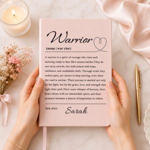 Peut inclure: Un carnet rose p&acirc;le pr&eacute;sentant la d&eacute;finition imprim&eacute;e du mot Warrior, une ic&ocirc;ne de c&oelig;ur en pointill&eacute;s et le nom Sarah sous la section See also. Le texte d&eacute;crit un esprit de courage, de r&eacute;silience et de foi dans une police noire claire.