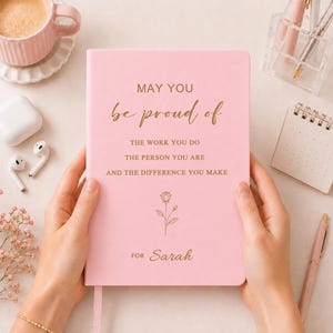 May include: A light pink hardback journal featuring gold foil text that reads: MAY YOU be proud of THE WORK YOU DO THE PERSON YOU ARE AND THE DIFFERENCE YOU MAKE, with a small gold rose illustration and the name Sarah printed at the bottom.