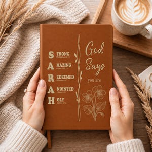May include: A brown notebook featuring the name SARAH vertically in large letters, with each letter starting a word: STRONG, AMAZING, REDEEMED, ANOINTED, and HOLY, accompanied by Bible verses. The cover also displays the text God Says you are.