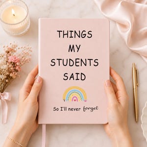 May include: A light pink notebook with the black text "THINGS MY STUDENTS SAID" printed on the cover. Below the text is a colorful rainbow illustration and the smaller black text "So I'll never forget" at the bottom of the front cover.