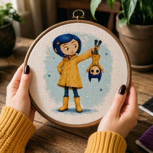 May include: A circular wooden embroidery hoop containing a cross-stitch design of a character with blue hair wearing a yellow raincoat and boots, holding a smaller inverted version of the same character by the feet against a light blue stippled background.