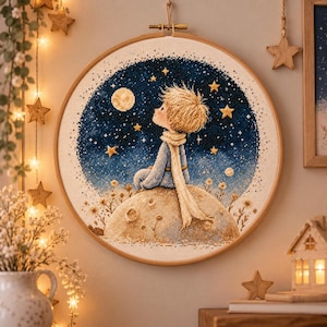May include: A circular wooden embroidery hoop containing a cross-stitch artwork of a young person with blonde hair wearing a long scarf, sitting on a cratered planet and looking up at a dark blue starry night sky with a glowing full moon.