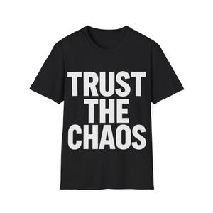 以下が含まれることがあります： 前面に白い「TRUST THE CHAOS」の文字がプリントされた黒いTシャツ。テキストは太字のサンセリフ体です。シャツはベーシックな半袖スタイルです。