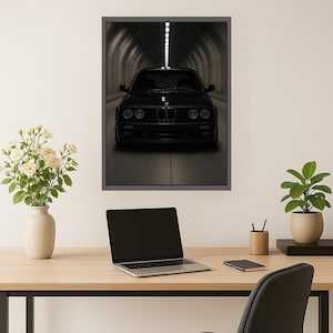 May include: Framed print of a black car in a tunnel. The car is centered, with headlights visible. The tunnel has a series of lights along the ceiling, creating a sense of depth. The print is displayed on a light-coloured wall above a wooden desk.
