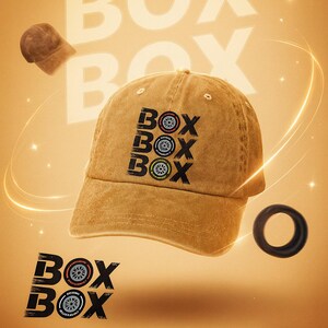 May include: Mustard-colored baseball cap with the word "BOX" in a stylized font, repeated multiple times. The design includes a tire graphic. A black tire and a floating cap are also visible against a golden background.