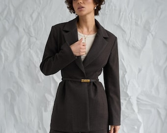 Pode incluir: Conjunto de blazer e calções castanho escuro. O blazer tem lapelas entalhadas e um cinto com fivela dourada. O conjunto é usado com um top creme. Os calções combinam com o blazer.
