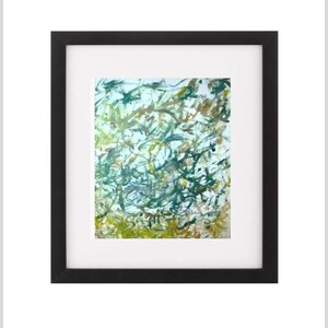 Puede incluir: Impresión de arte abstracto en un marco negro. La obra presenta una mezcla de pinceladas verdes, amarillas y marrones sobre un fondo blanco. La pintura está enmarcada con un passe-partout blanco.