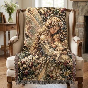 May include: A woven throw blanket featuring a detailed tapestry design of a winged figure with long hair holding a small child. The scene is surrounded by intricate floral and berry patterns in shades of gold, green, red, and white with fringe.