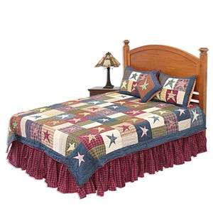 May include: A bed with a patchwork quilt featuring star and plaid patterns in red, blue, green, and cream. The bed has matching star-patterned pillows, a red plaid bed skirt, and a wooden headboard. A lamp sits on a nightstand.
