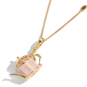 May include: Gold-coloured necklace with a pink teapot pendant. The teapot has a gold handle, spout, and lid, with a decorative design on the front. The lid is embellished with small, clear stones. The chain is delicate and gold.