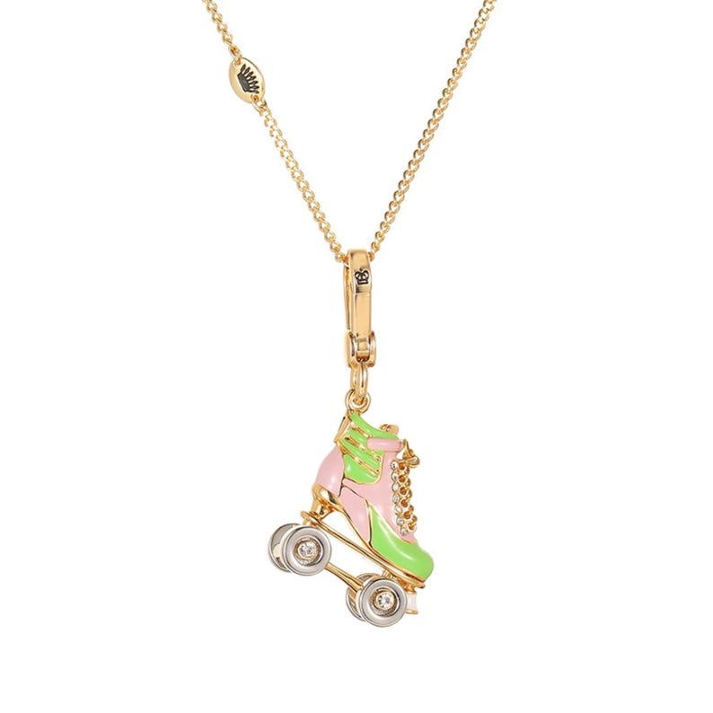 May include: Gold-tone necklace featuring a roller skate pendant. The pendant is pink and green with silver-tone wheels and a small chain. The necklace has a delicate chain and a lobster clasp.