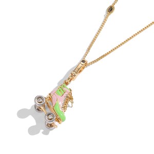 May include: A gold-colored necklace featuring a pendant shaped like a roller skate. The skate is pink and green with silver wheels and clear gem accents. The chain is delicate and has a lobster clasp.