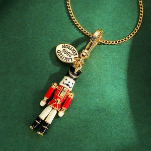 May include: A gold-coloured necklace with a charm depicting a miniature nutcracker soldier. The nutcracker wears a red coat, black hat, and white trousers. The charm includes a small, gold-coloured tag that reads "LIMITED EDITION 2006".